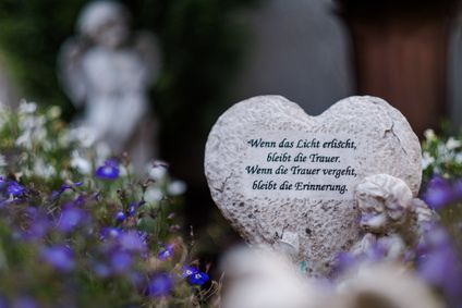 Foto des herzförmigen Gedenksteins im Friedhof, umgeben von Blumen